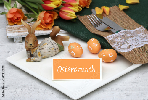Text Osterbrunch auf einer Tischkarte mit Besteck Blumen und Ostereiern.	