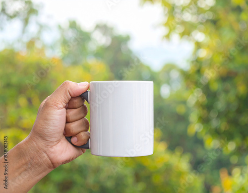 Hand Holding a White Mug Against a Blurred Green Nature Background