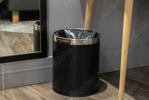 Modern black waste bin with metallic rim and a trash bag on a wooden floor, symbolizing cleanliness and efficient waste management in an interior