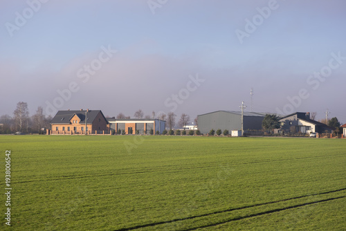 Expansive green agricultural field leading to modern residential homes and commercial buildings under a clear sky, depicting rural development and land use