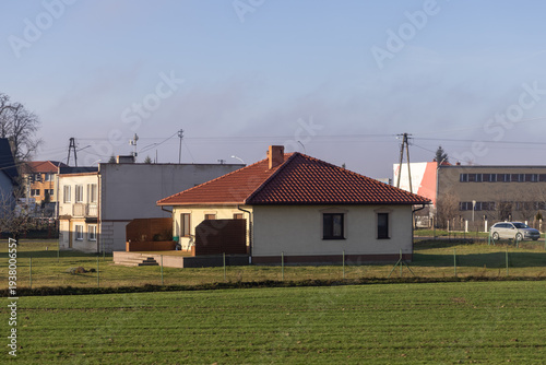 A quaint residential home with a vibrant red tiled roof and lush green field, symbolizing peaceful suburban life and accessible property ownership