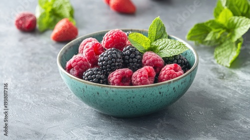 A ceramic bowl filled with a mix of raspberries, blackberries, and strawberries. Fresh mint leaves are arranged around the bowl.