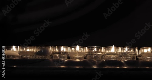 Burning tealights in clear holders on a marble altar ledge, steady view shows gentle flicker and warm glow as melted wax and tiny wicks catch the only light inside the church gloom