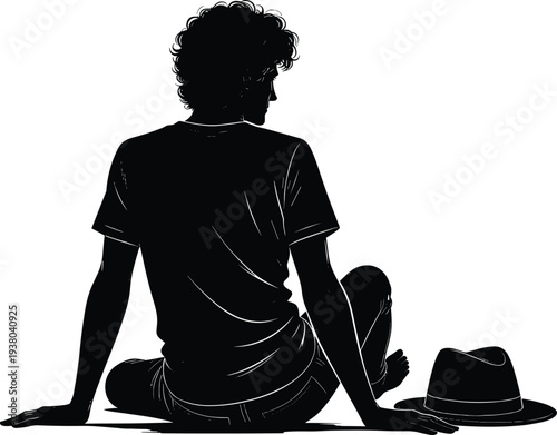 Back view silhouette of a young man with curly hair sitting on the ground with a fedora hat beside him