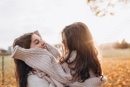 Photography Mother and daughter wearing cozy knitted sweaters share warm embrace outdoors during golden-hour in autumn