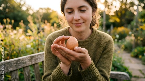 A young woman in a green sweater gently holding a brown egg in her hands outdoors in a garden during daytime