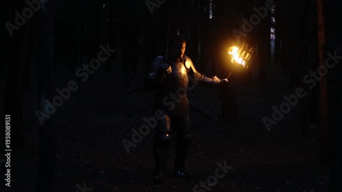 A knight in full armor, his face bloodied and scarred, holding a sword and torch, is sneaking through a dark night forest. A medieval warrior searches in the darkness.