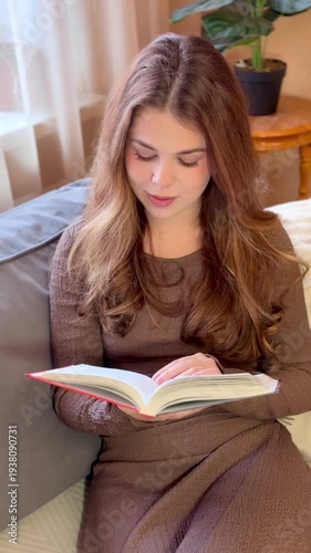 Beautiful young girl reading a book at home lying on the sofa in silence