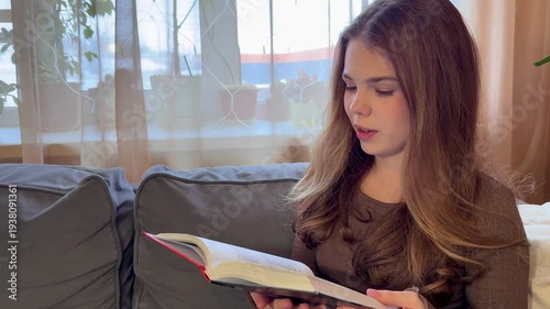Beautiful young girl reading a book at home lying on the sofa in silence