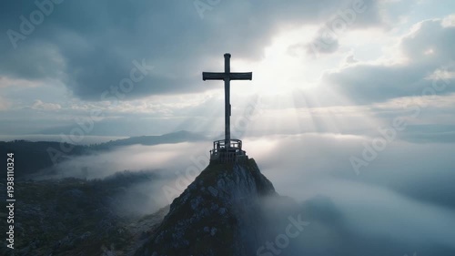 Majestic cross on a mountain peak above a sea of clouds. Sunlight beams through the dramatic sky creating a spiritual scene. Concept of faith hope and resurrection