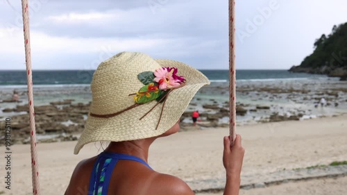 A woman seated on a coastal swing enjoys the coastal breeze on a tropical island.