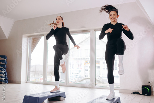 Two women doing a high-intensity step aerobics workout in a bright fitness studio together