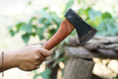 Foto Close up of a hand holding a sharp hatchet with wooden handle near a chopping block and stacked logs outdoors