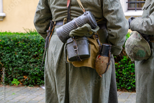 Photography Historical military equipment on a soldier's belt: metal gas mask canister, canteen in cover, mess tin and bayonets – detail of a World War II reenactment uniform during outdoor event