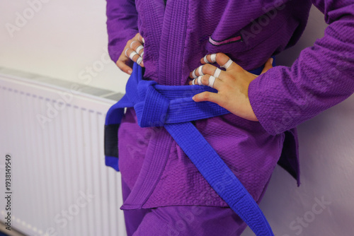 Billede på lærred Woman in a purple martial arts gi with a blue belt standing with hands on her hi