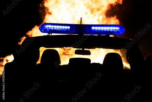 firefighter or policeman near your vehicle with emergency strobe lights in silhouette  watching fire out of control at night