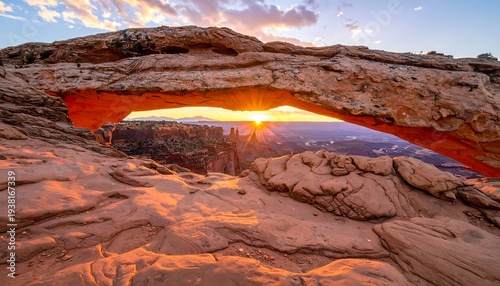 Sunrise through sandstone arch framing distant canyon landscape, creating dramatic sky hues & depth