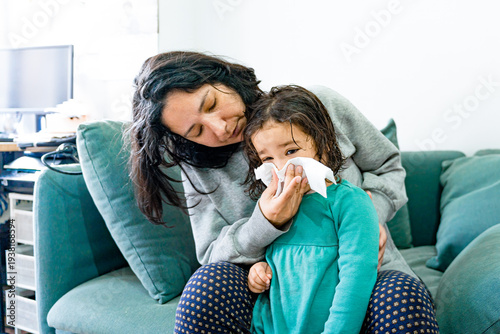 young millennial mother sneezing sick child nose, taking care of toddler with flu or cold at home, motherhood