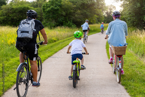 Foto Family children cycling paved countryside path green meadow trees during warm summer day light