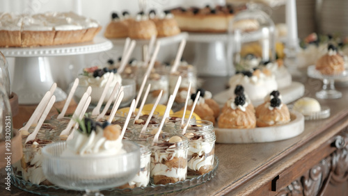 Elegant dessert buffet featuring assorted miniature pastries, cakes, and cream-filled glass jars on a rustic wooden table
