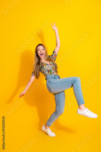 Wallpaper Mural Young woman jumping in bright yellow studio wearing floral top jeans and sneakers enjoying fashion lifestyle Torontodigital.ca