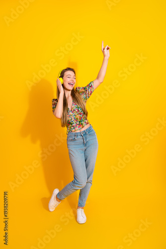 Wallpaper Mural Young woman dancing with headphones against bright yellow background wearing floral top and jeans for lifestyle fashion and music vibe Torontodigital.ca