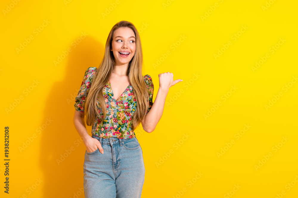 Naklejka premium Young chic woman in floral top and jeans smiles against a bright yellow background