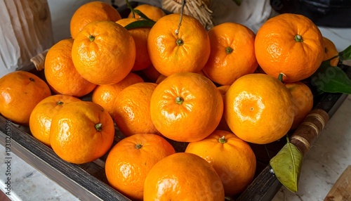 Tray overflowing with bright orange citrus fruits, some with green leaves, against a light marble countertop
