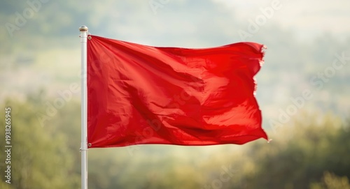 Close capture of a dynamic red flag fluttering over a softly blurred natural setting including copy space