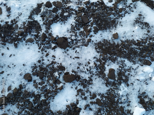 Dark earth texture with scattered snow. Winter soil background