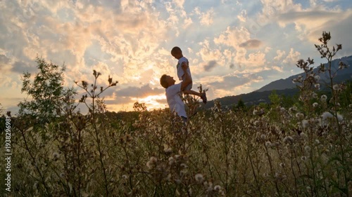 A father holds his son in his arms and circles around at sunset.