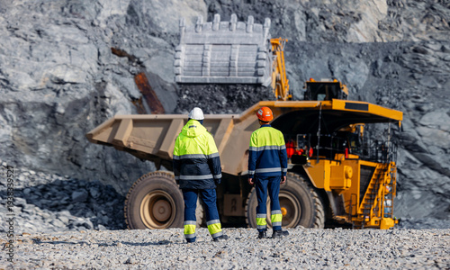 Φωτογραφία Work team engineers supervise loading of gold ore by excavator into large quarry yellow truck