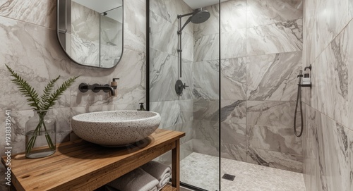 Chic bathroom setup including a stone basin placed on a rustic wooden base, a glass shower screen and walls adorned with marble look tiles