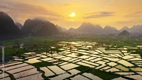 Scenic aerial view of limestone karst mountains and flooded rice paddies reflecting golden sunset light in Guilin, China.