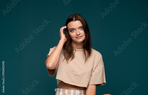 Young woman smiling, hand running through hair, brunette girl showing natural beauty against teal background