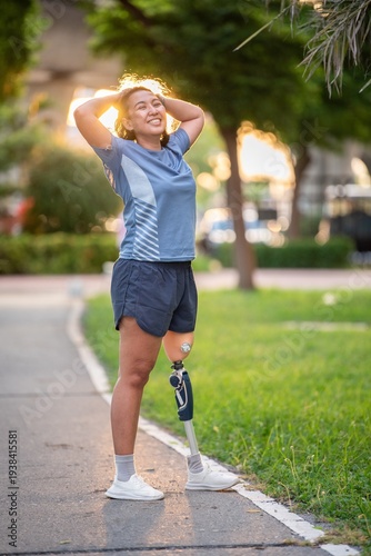Happy woman with prosthetic leg smiling and enjoying after exercise in park at sunset. Confident female amputee with lower artificial limb posing outdoors living joyful life in nature.