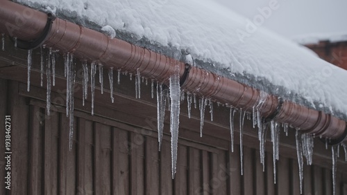 Long Hazardous Icicles Hanging from Frozen Rain Gutter Over Street Sidewalk Posing Injury Danger for Pedestrians