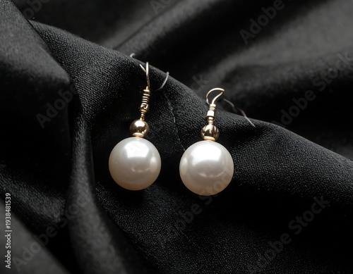 Two lustrous pearl drop earrings resting on a draped black fabric background, captured in elegant studio lighting