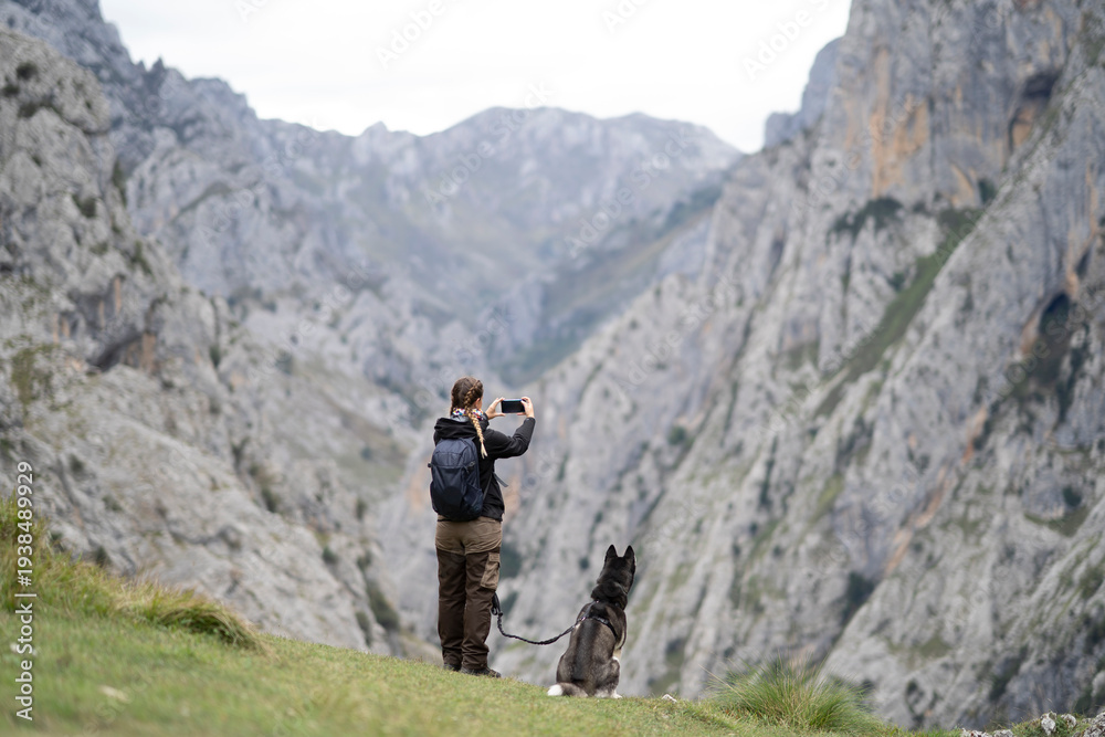 Fototapeta premium Woman hiking with dog photographing picos de europa mountains