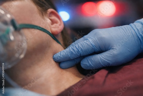 A gloved hand checks the pulse of a patient wearing an oxygen mask. The scene depicts an urgent medical emergency with blurred ambulance lights. Ideal for healthcare and safety articles.