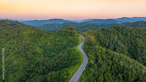 Aerial view of a scenic winding mountain road cutting through lush green hills in Nan, Thailand. The dramatic curves form the shape of the number three, making it a popular tourist attraction