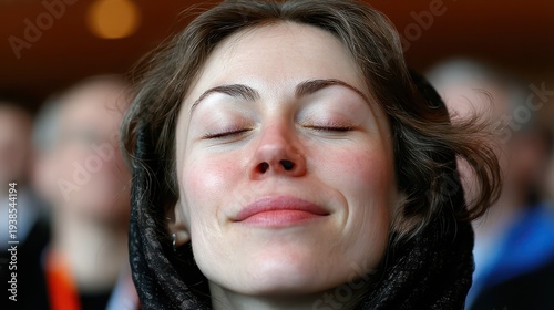 A young woman smiles serenely, her eyes closed in deep contemplation, at an indoor event. Her peaceful expression captures a moment of quiet joy and profound connection