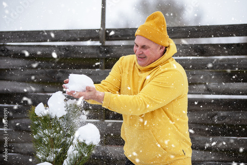 Man in yellow hoodie plays with snow outside, enjoying winter season
