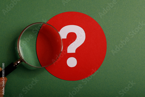 Fotografi Close-up of magnifying glass examining a red question mark on green background,