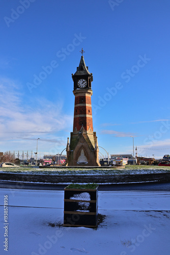 Skegness Jubilee Clock Tower surrounded by soft winter snowfall under blue sky; historic seaside landmark on Lincolnshire coast in seasonal setting with fresh snow, England, UK
