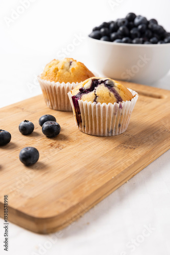 Two Homemade Blueberry Muffins on Bamboo Cutting Board with Fresh Blueberries