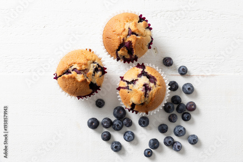 Overhead View of Three Homemade Blueberry Muffins with Fresh Blueberries on White Surface