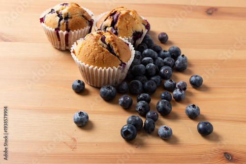 Three Homemade Blueberry Muffins with Scattered Fresh Blueberries on Wooden Table, Horizontal