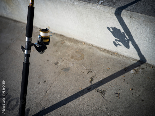 Fishing rod in the sun propped against a wall and fence