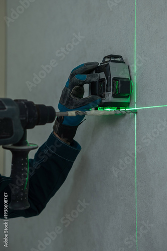 A man measures distances with a laser level and drills into a wall with a hammer drill.